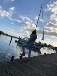 Man sitting on pier by sea against sky