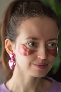 Woman with pink patches in heart shape under eyes and in heart earrings. skin care, valentines day.