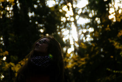 Low angle view of young woman standing against trees