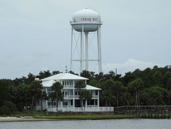 Water tower by lake against sky