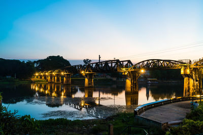 Illuminated bridge over river against sky at sunset