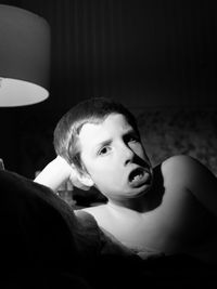 Portrait of shirtless boy making face while lying on bed at home