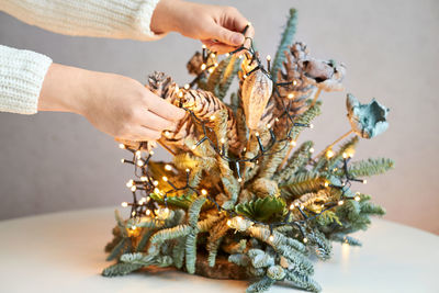The girl's hands decorate the christmas decoration from fir branches with a garland of lights.