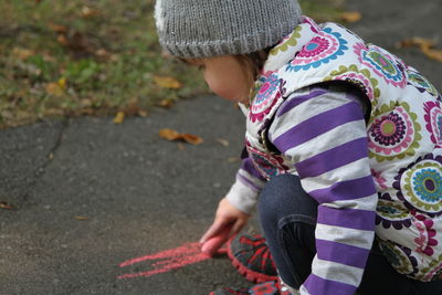 Side view of girl drawing on road with chalk during autumn