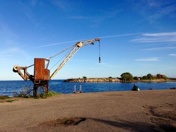 Crane on pier by sea against blue sky