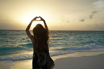 Silhouette woman standing at beach against sky during sunset