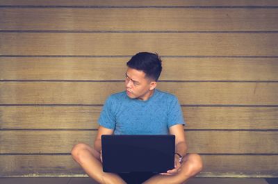 Young man using mobile phone while sitting on wood