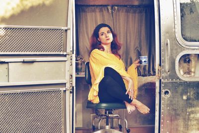 Beautiful young woman drinking coffee while sitting on chair