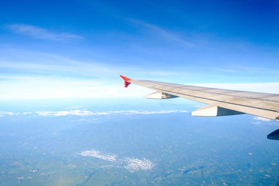 Airplane wing over landscape against blue sky