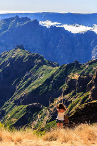 Rear view of woman standing on cliff against mountains