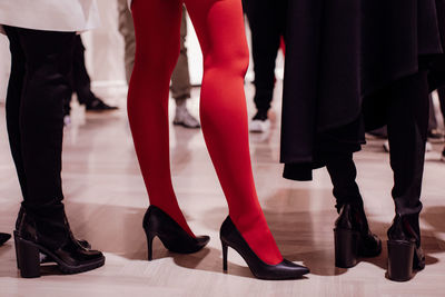 Fashion models on backstage dressed in a black long skirt, red tights and high heels.