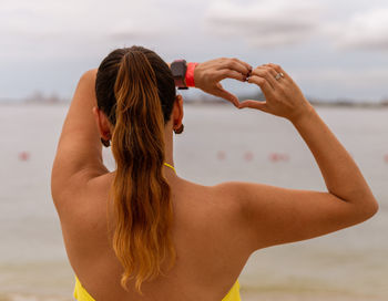 Rear view of woman with arms raised standing at beach