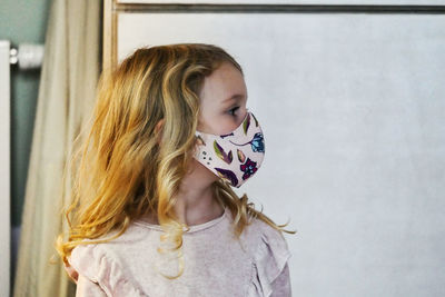 Close-up of cute girl wearing mask standing at home
