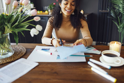 Smiling young woman making scrapbook at home