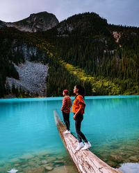 Rear view of friends standing by lake against mountain