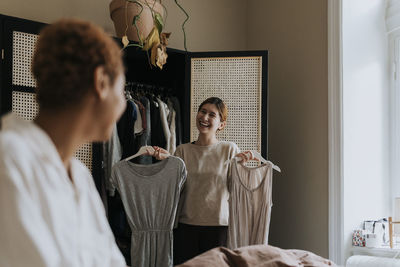 Happy non-binary person holding dress while standing near wardrobe at home