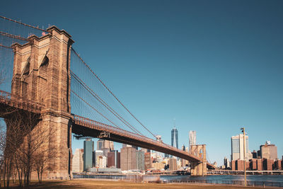 Low angle view of brooklyn bridge over river against clear blue sky in city