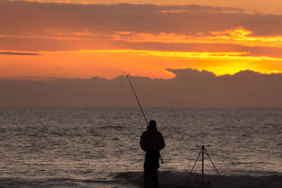 Man fishing in sea at sunset