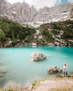 Rear view of woman standing on rocks in lake against mountains