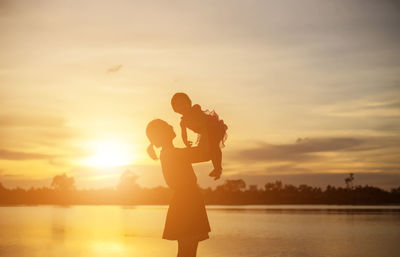 Silhouette people standing on shore against sky during sunset