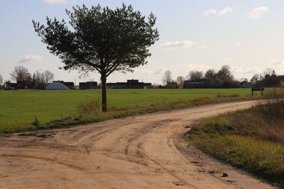 Dirt road amidst field against sky