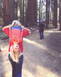 Rear view of parents piggybacking children while walking on footpath in forest