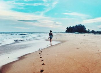 Rear view of woman walking on shore at beach