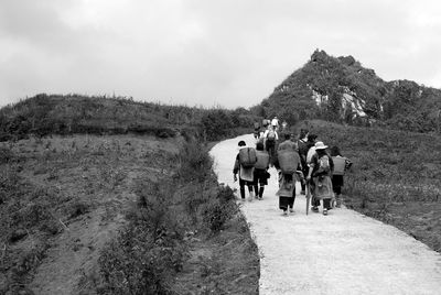 Rear view of people walking on footpath amidst field