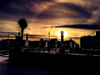 Silhouette city street and buildings against sky at sunset