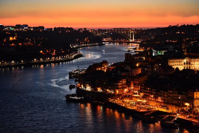 High angle view of illuminated buildings by river against sky at sunset