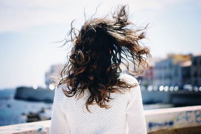 Rear view of woman with tousled hair against sky