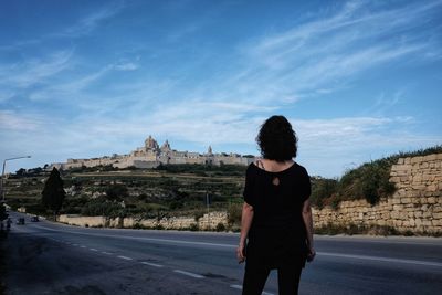 Rear view of woman standing on road while looking at historical building