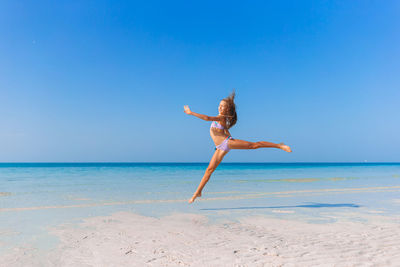 Full length of girl jumping on beach against sky