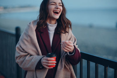 Young woman standing by railing against sea