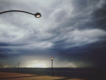 Low angle view of illuminated street light at beach against cloudy sky