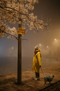 Woman with pug standing on sidewalk at night during winter