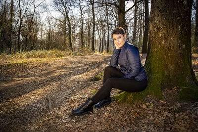 Young woman is sitting at the foot of an oak tree in the woods. 