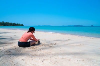 Young asian woman building sandcastle at the beautiful beach of island on summer vacation