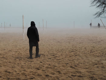 Rear view of man walking on beach during fog 