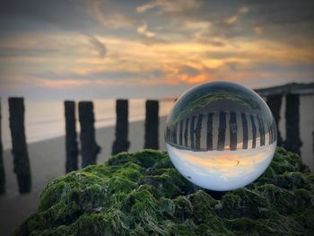 Close-up of wooden post on beach against sky during sunset