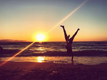 Silhouette man doing handstand at beach against sky during sunset