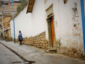 Rear view of man walking on footpath amidst buildings