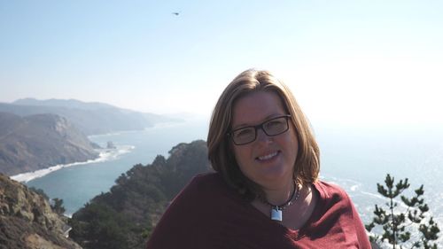 Portrait of smiling young woman standing on mountain against clear sky