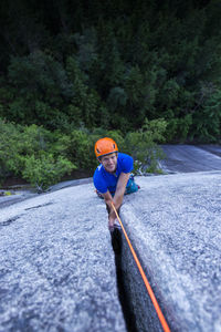 Man smiling and looking up at camera while climbing off width squamish