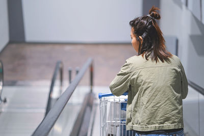 Rear view of woman standing on moving walkway at supermarket