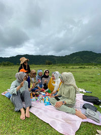 Friends sitting on field against sky