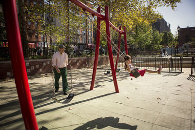 Grandfather looking at granddaughter sitting on swing in park