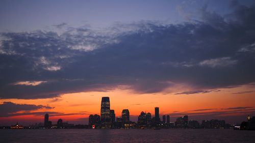 Sea by buildings against sky during sunset