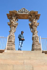 Low angle portrait of man standing at entrance of temple against clear blue sky