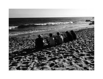 Rear view of people sitting on beach against clear sky